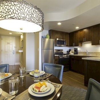 A modern kitchen and dining area with dark wood cabinets, stainless appliances, a round pendant light, and a table set for four.