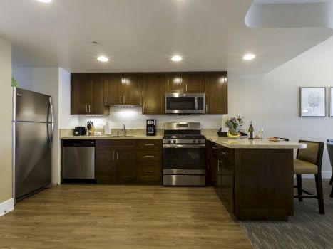 A modern kitchen with dark wood cabinets, stainless steel appliances, a center island, and a small dining area nearby.