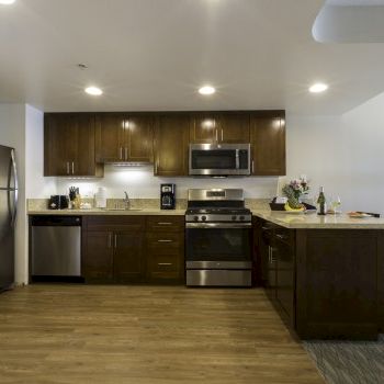 A modern kitchen with dark wood cabinets, stainless steel appliances, a small island, and a breakfast bar; wood flooring and soft lighting.